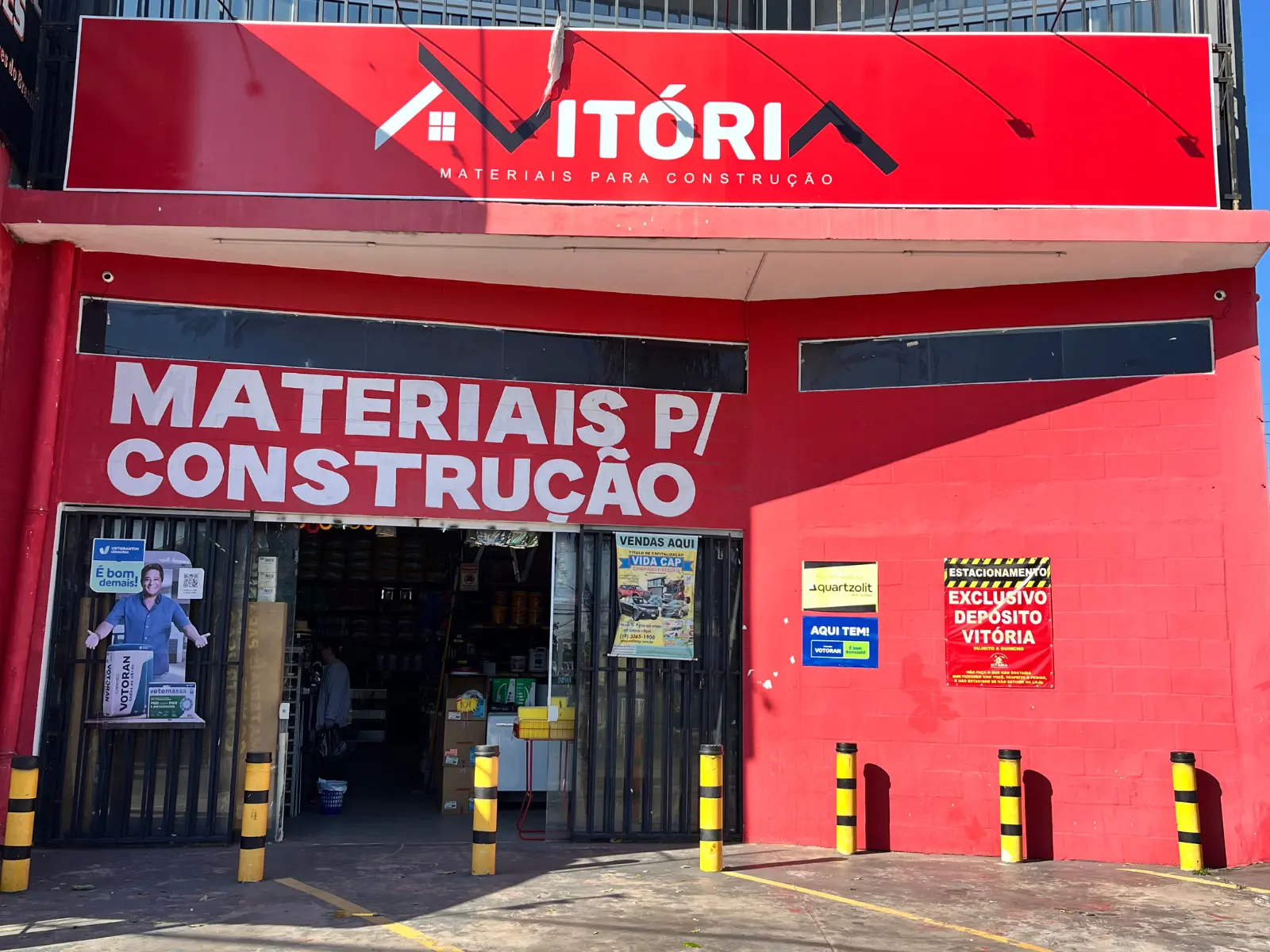 Fachada do Depósito Vitória, com letreiro vermelho "Vitória Materiais para Construção" e a entrada da loja, no DIC V, em Campinas/SP.